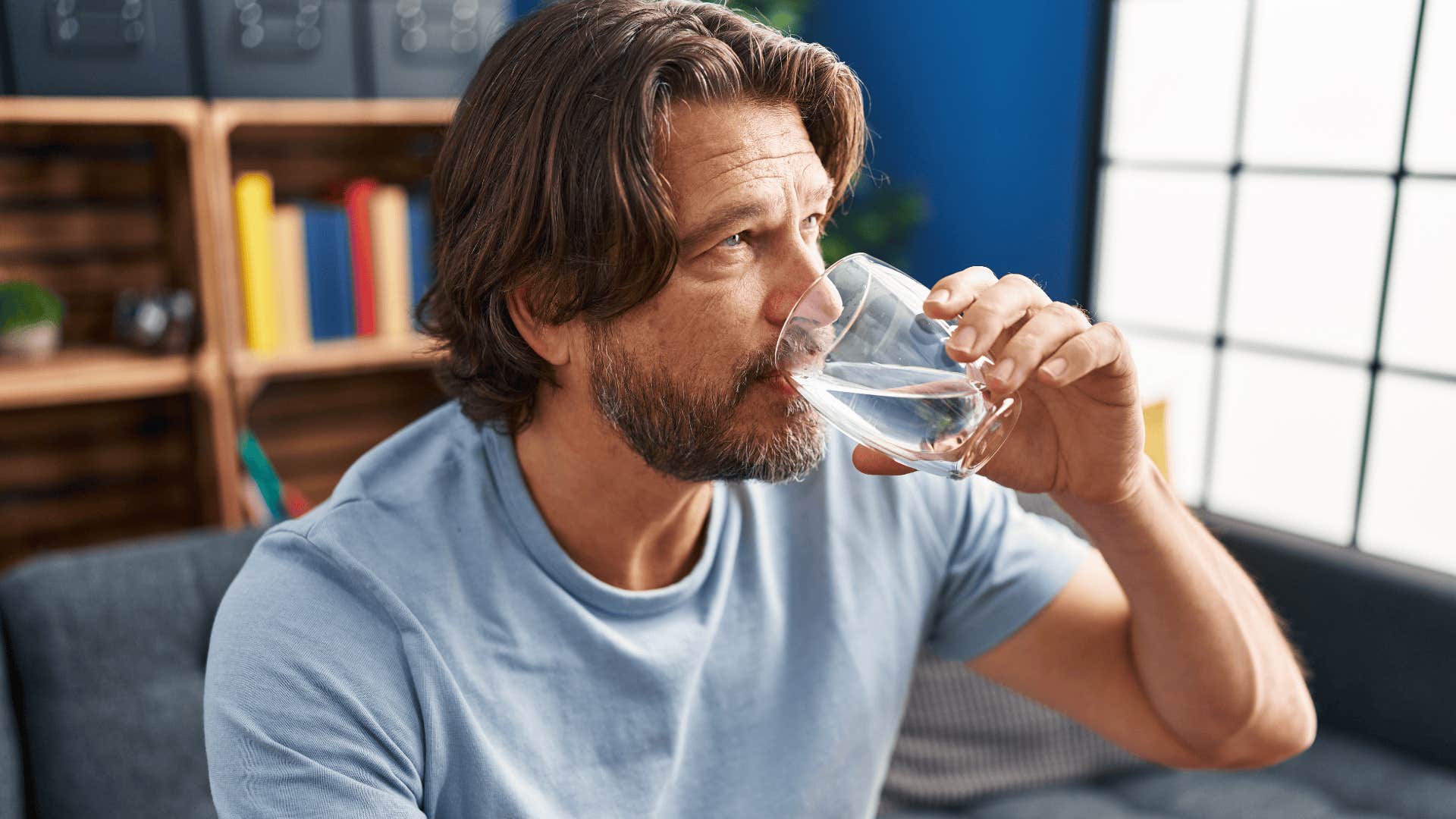 Middle age man drinking glass of water sitting on sofa at home