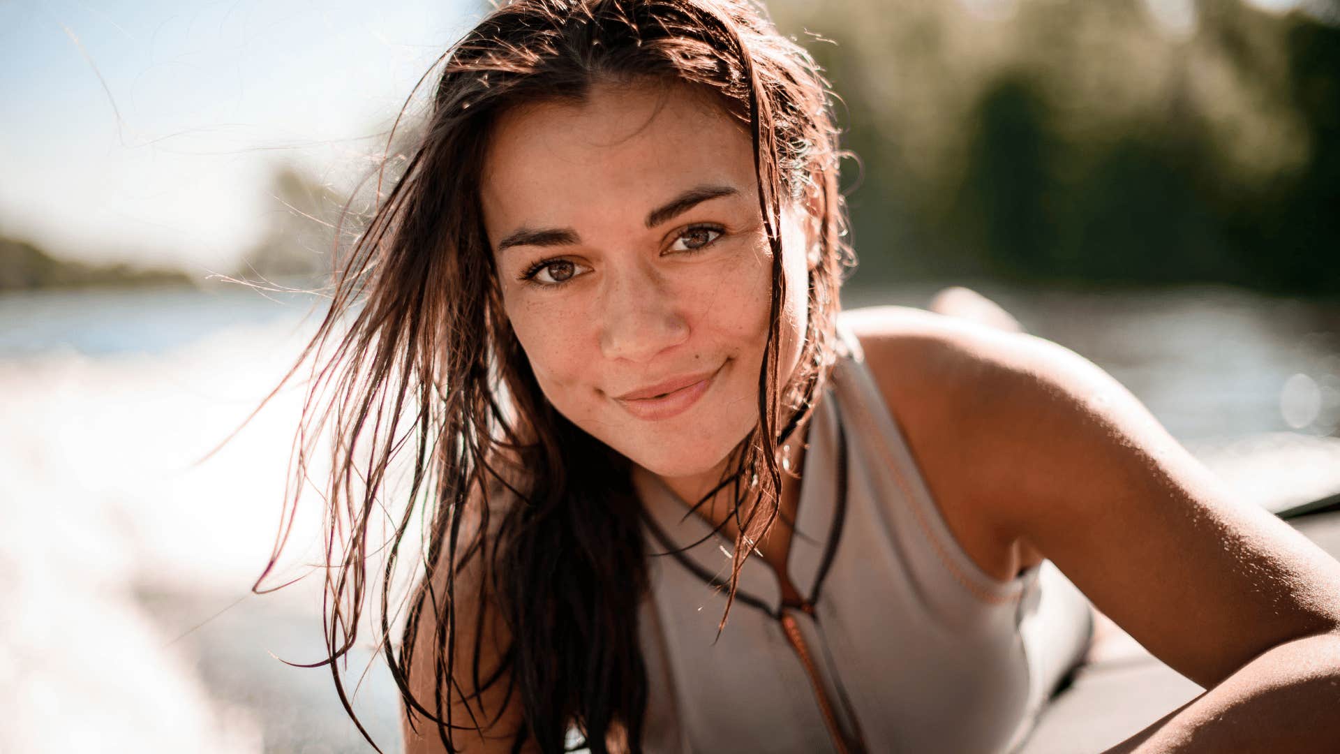 Portrait of young smiling woman with brown eyes and wet hair on blurred background beach