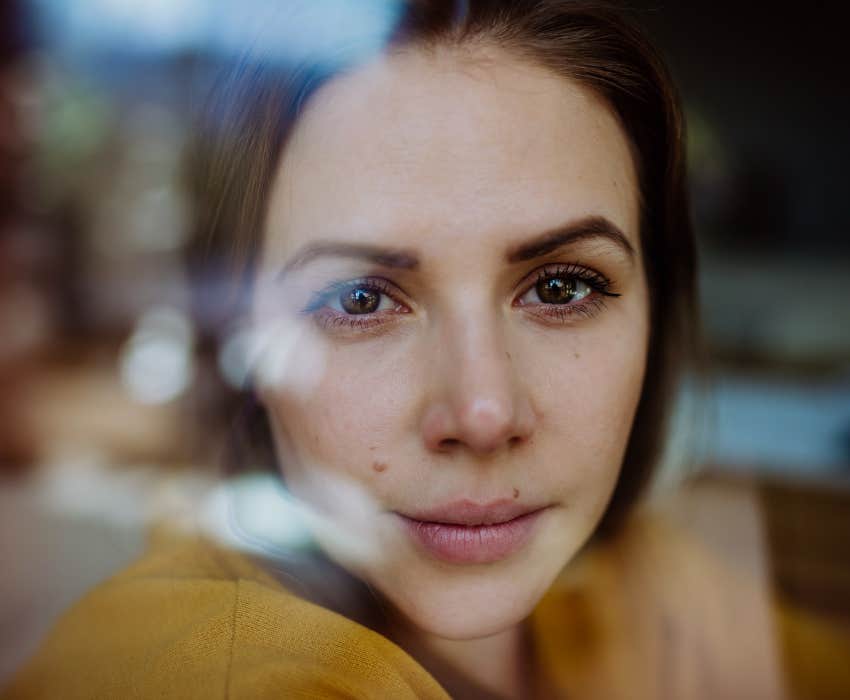 Close-up portrait of woman looking through window.