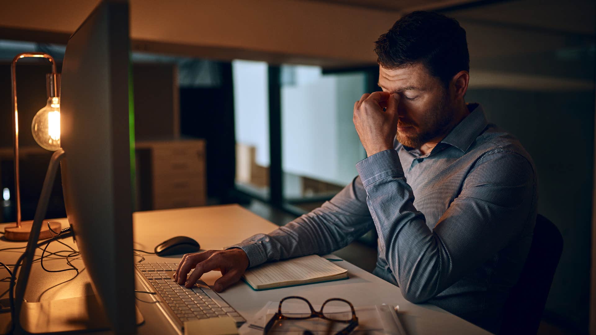 Man holding his head looking tired in a dark office.