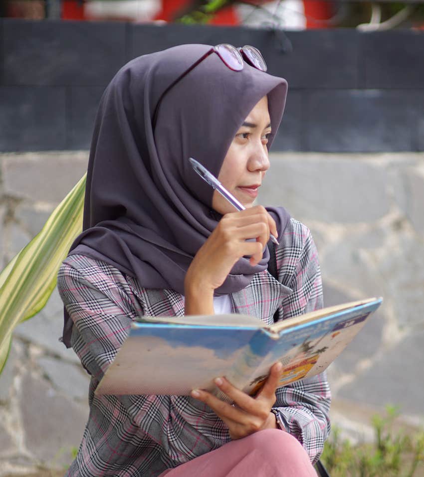 Woman sits in garden and writes ideas in a notebook