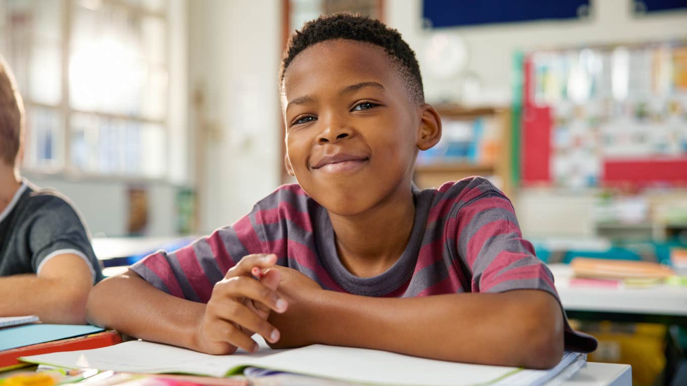 happy black elementary boy studying in classroom while looking at camera