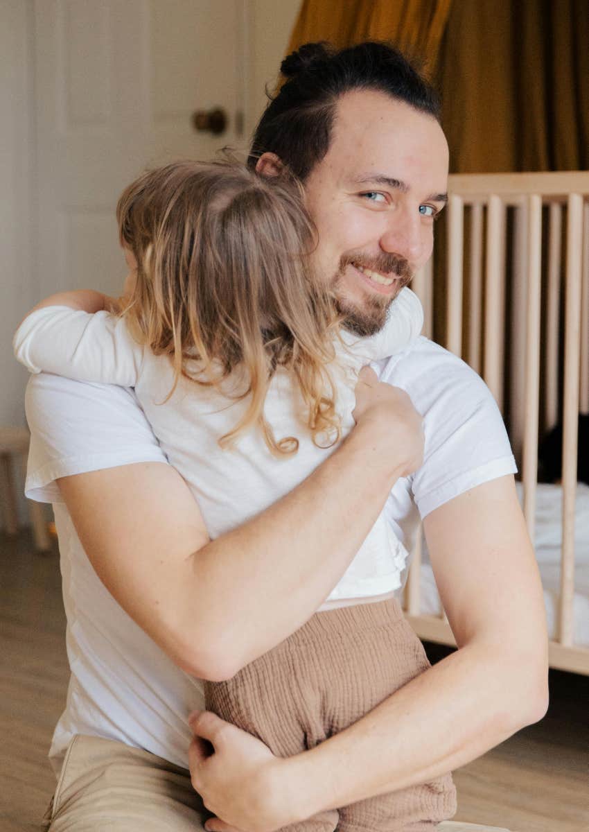 father smiling while hugging his young daughter