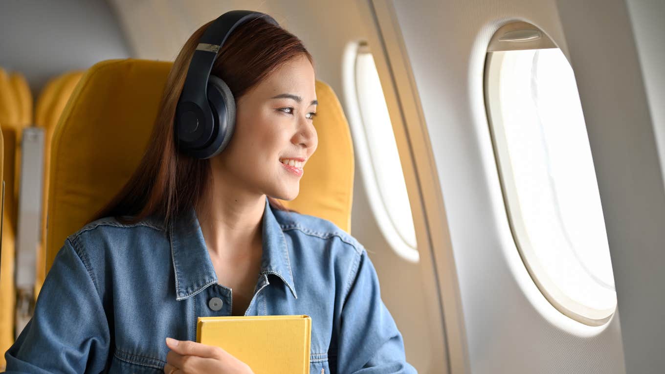 Gen Z traveler smiling while looking out plane window