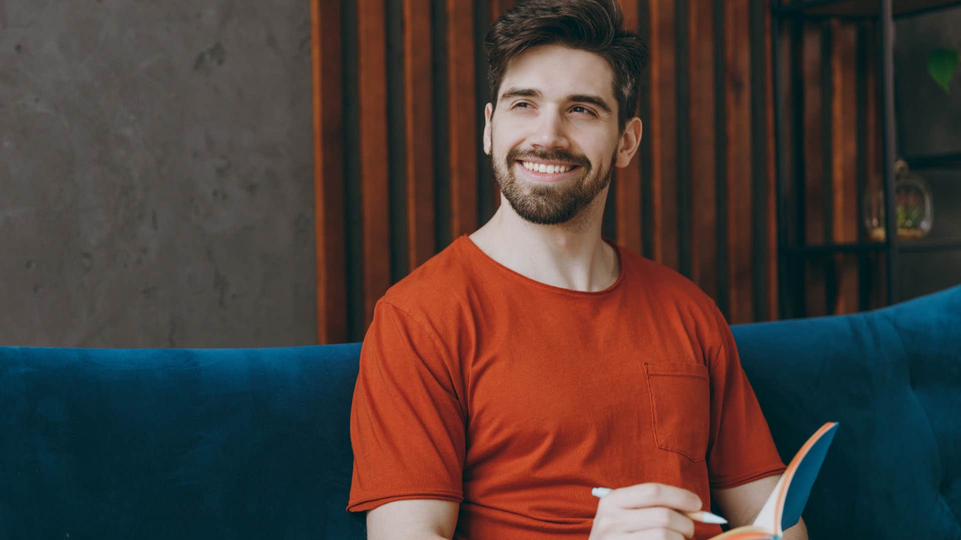 Man smiling while writing in his journal on the couch.