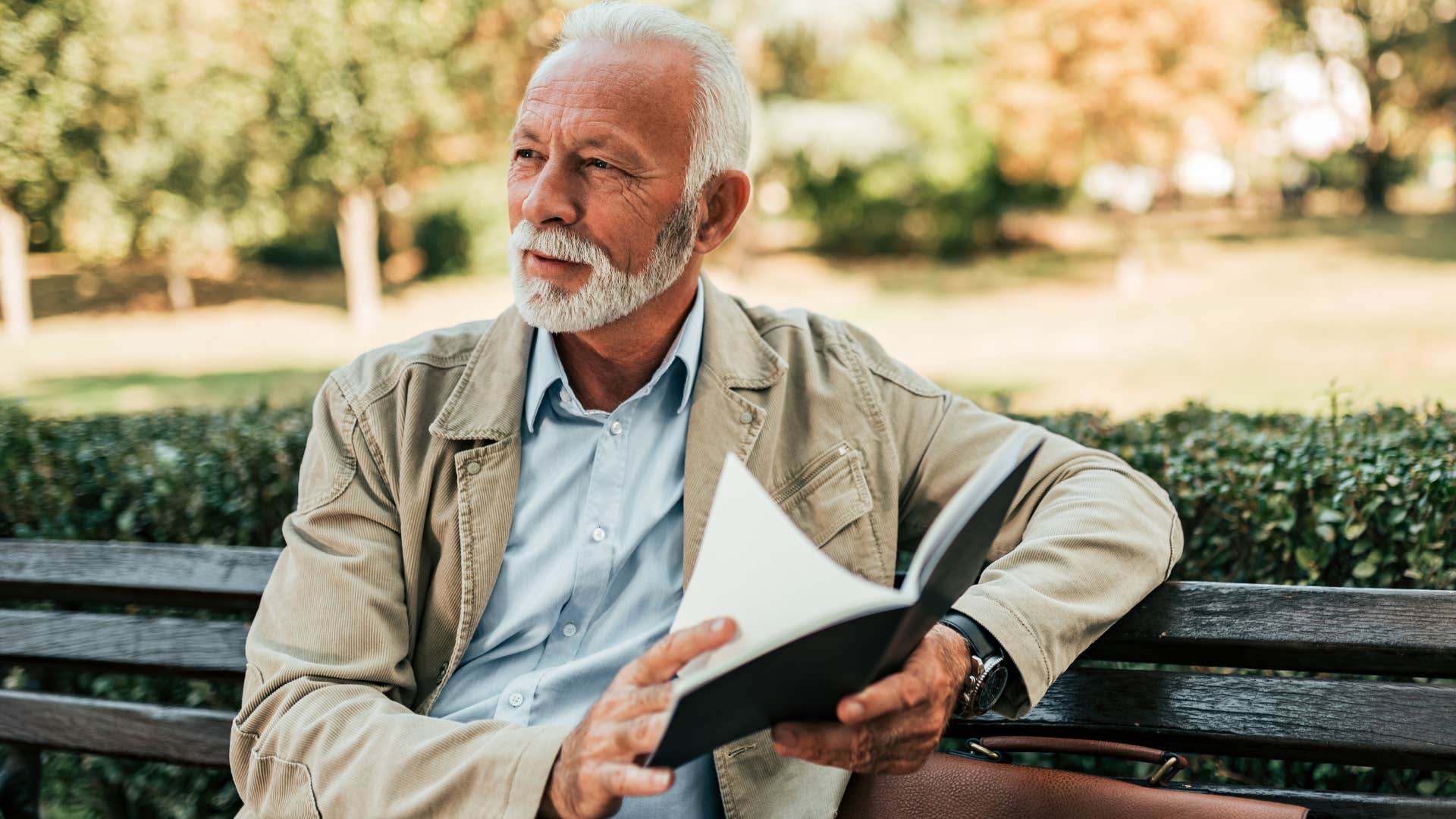 Older man smiling while reading on a park bench.