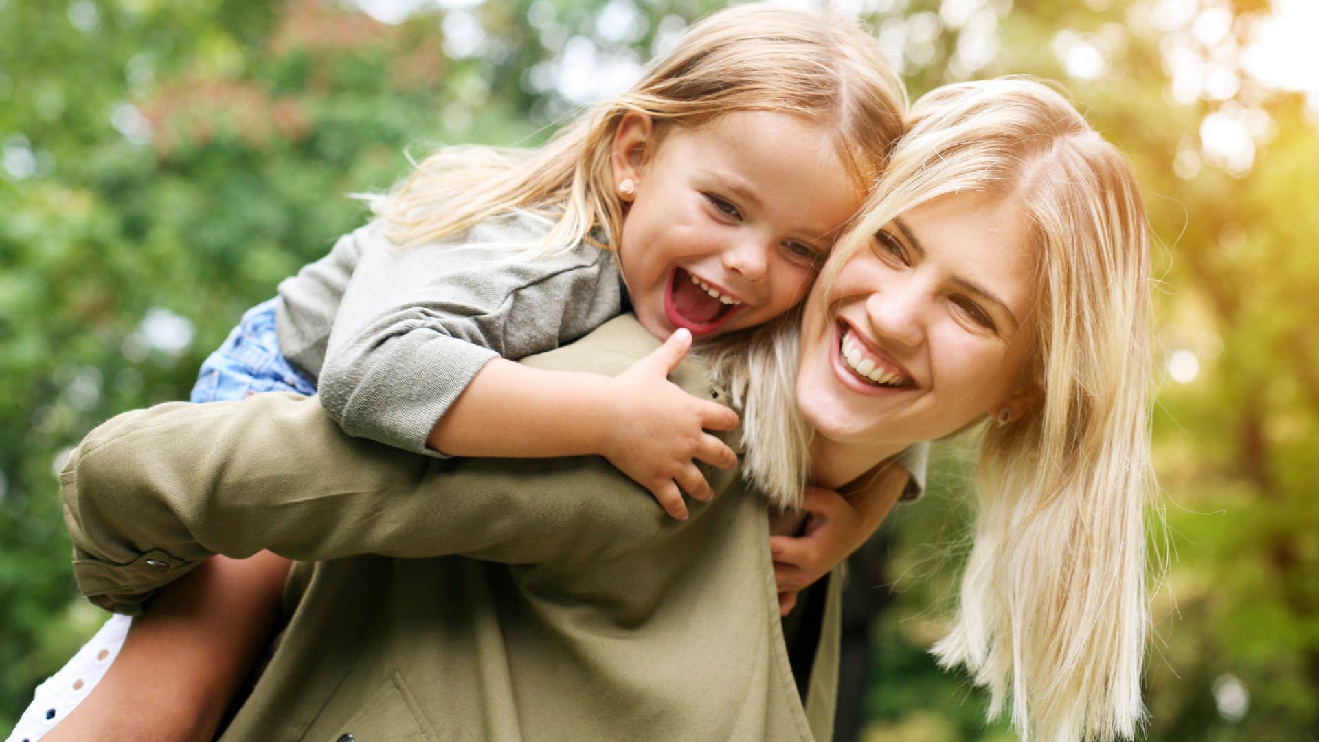 Woman smiling while holding her younger daughter on her back.