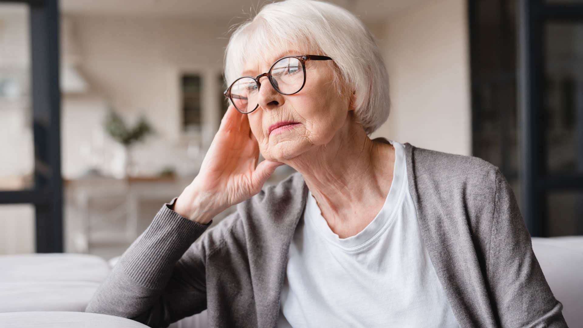 Older woman looking sadly out her window.