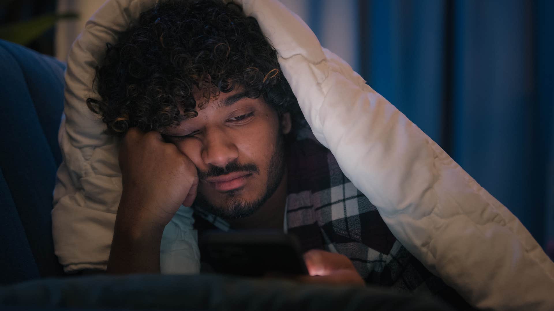 Man scrolling on his phone from bed.