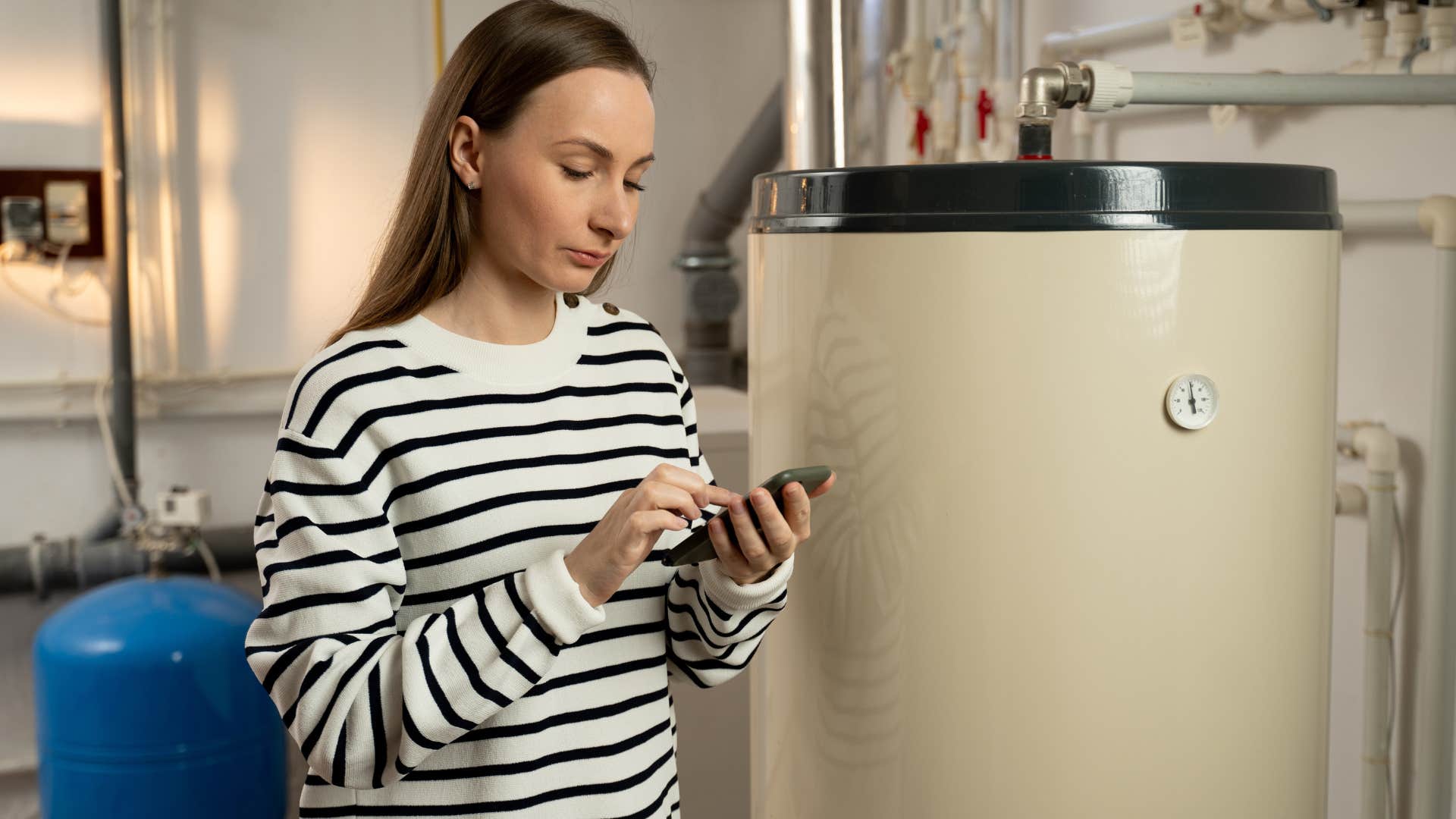 Young woman texting in front of her water heater.