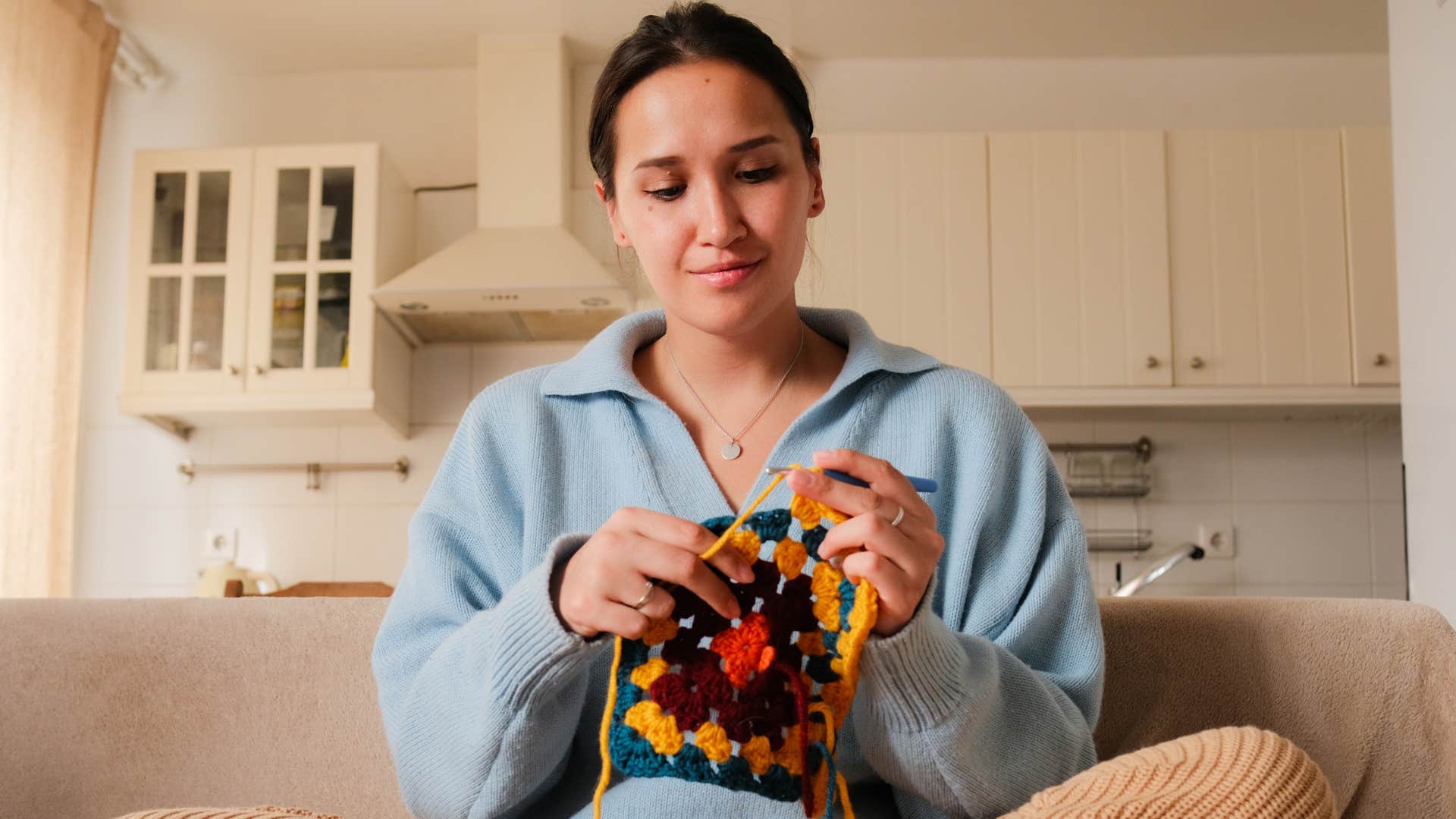 Young woman smiling and crocheting on her couch