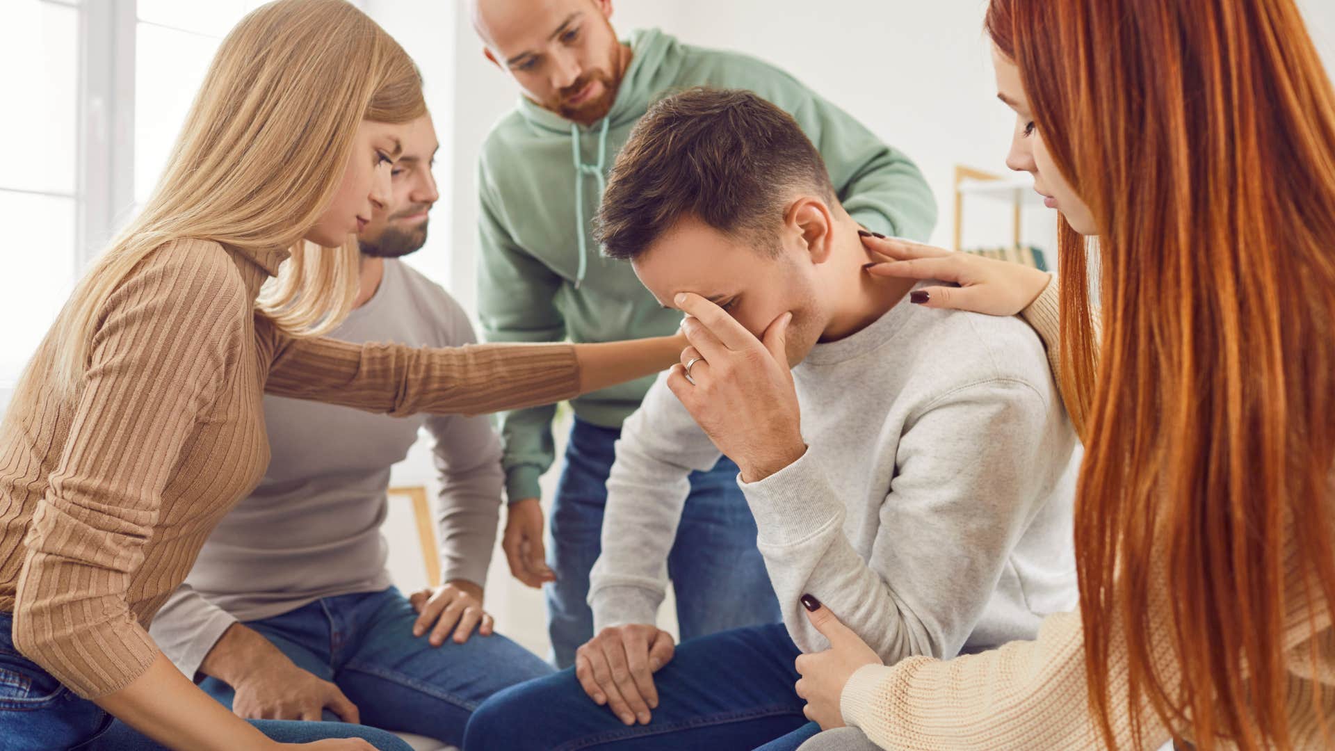 A group of friends gathered together, setting up an intervention to talk to their friend about his romantic relationship