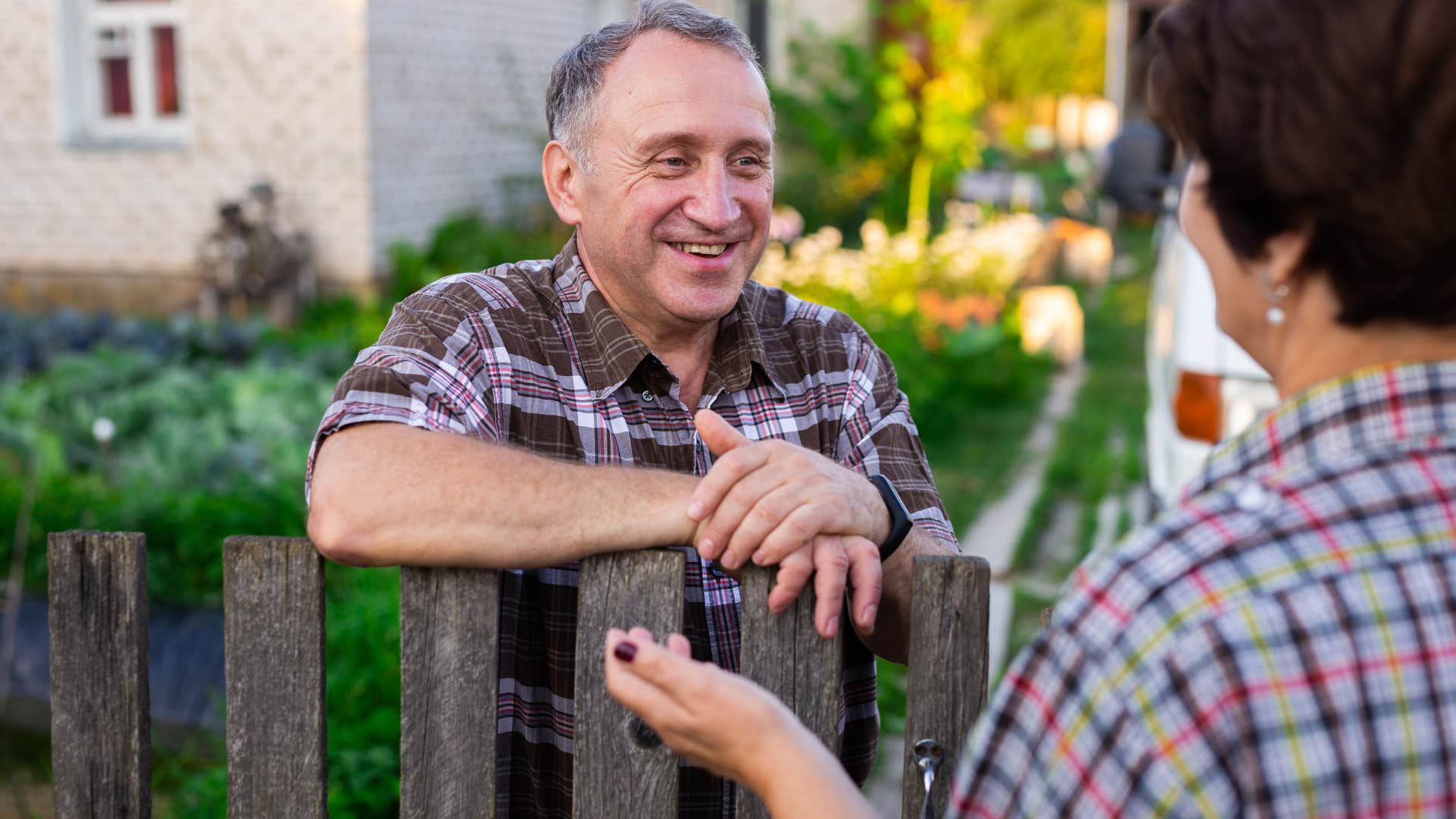 Older man smiling and talking to his neighbor over a fence