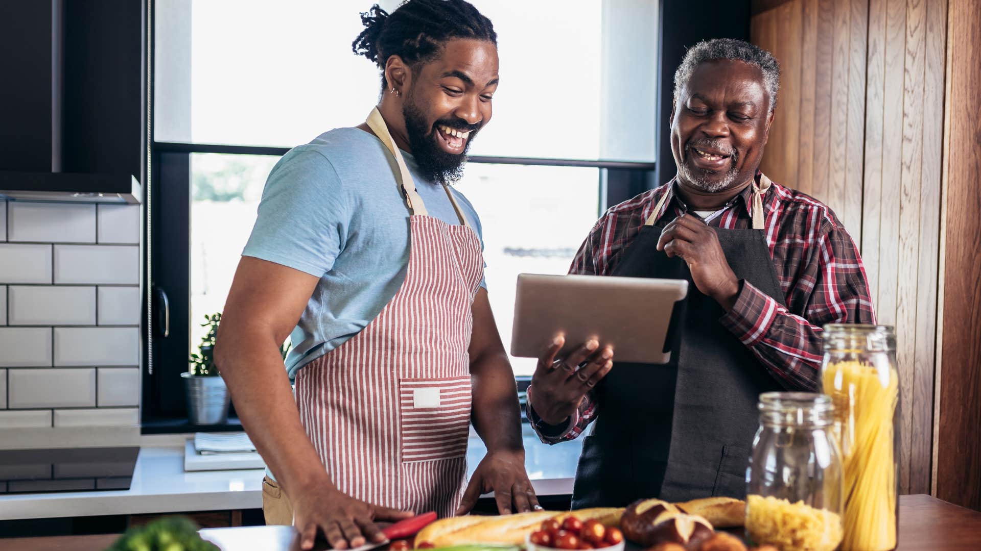 Father and adult son smiling and cooking together in a kitchen