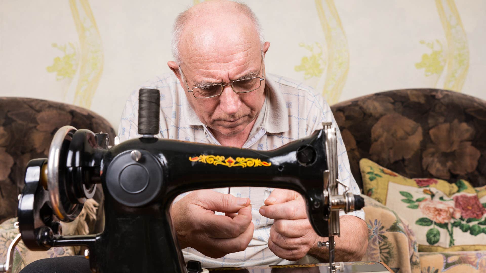 Older man threading a needle in front of his sewing machine