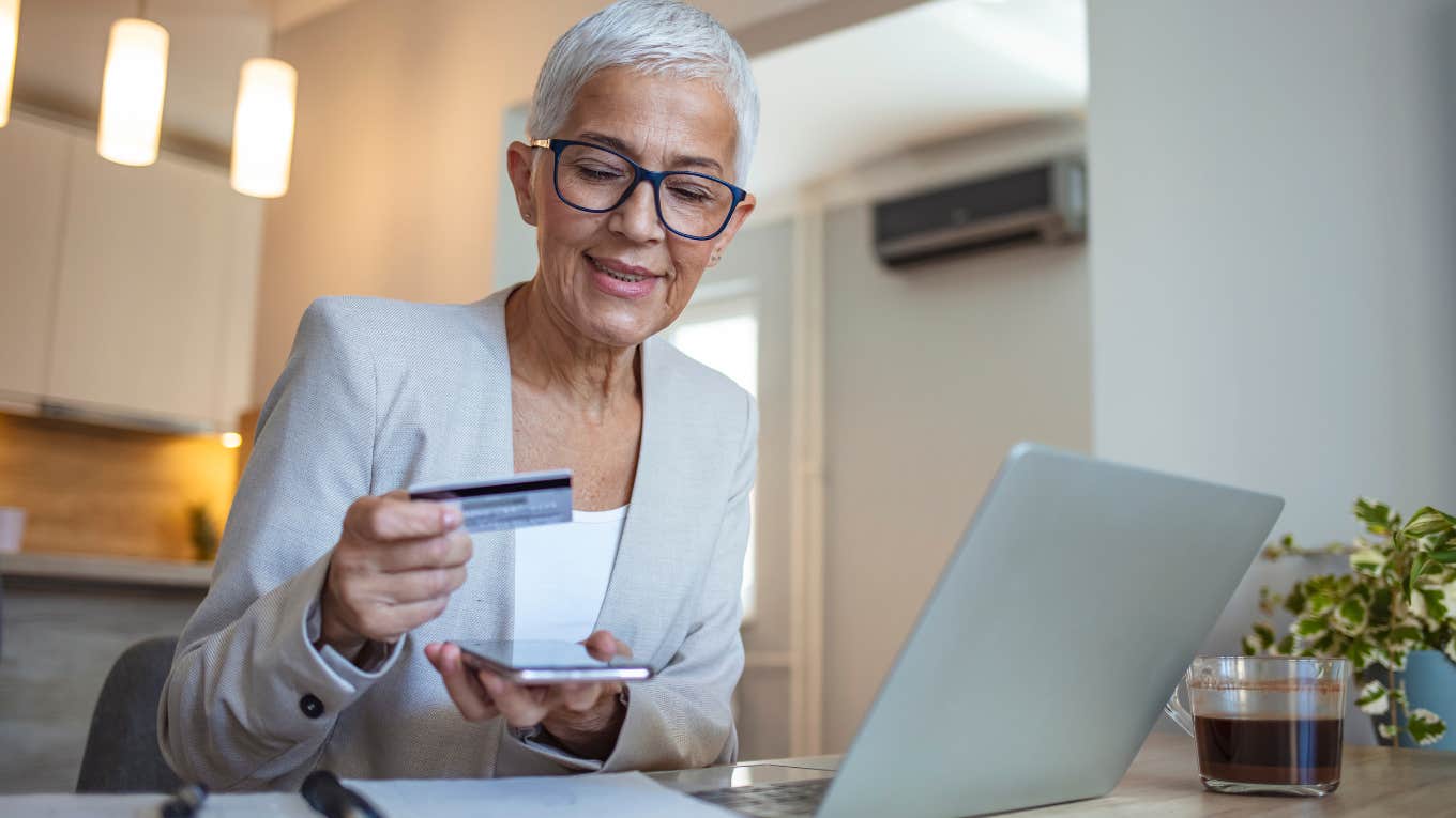 Older woman smiling and doing bills on her laptop.