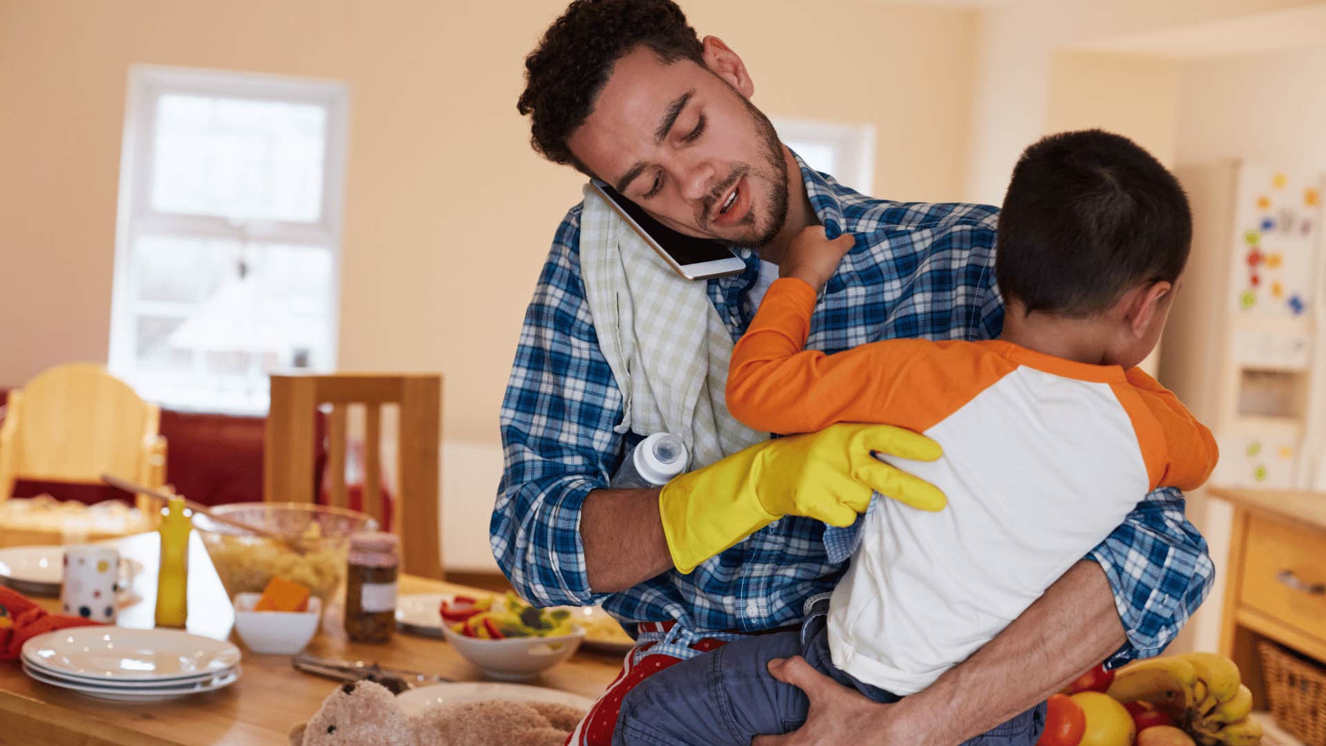 Busy father holds child in kitchen while talking on phone