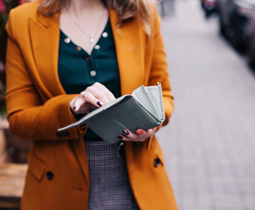 woman in orange suit jacket opening her wallet