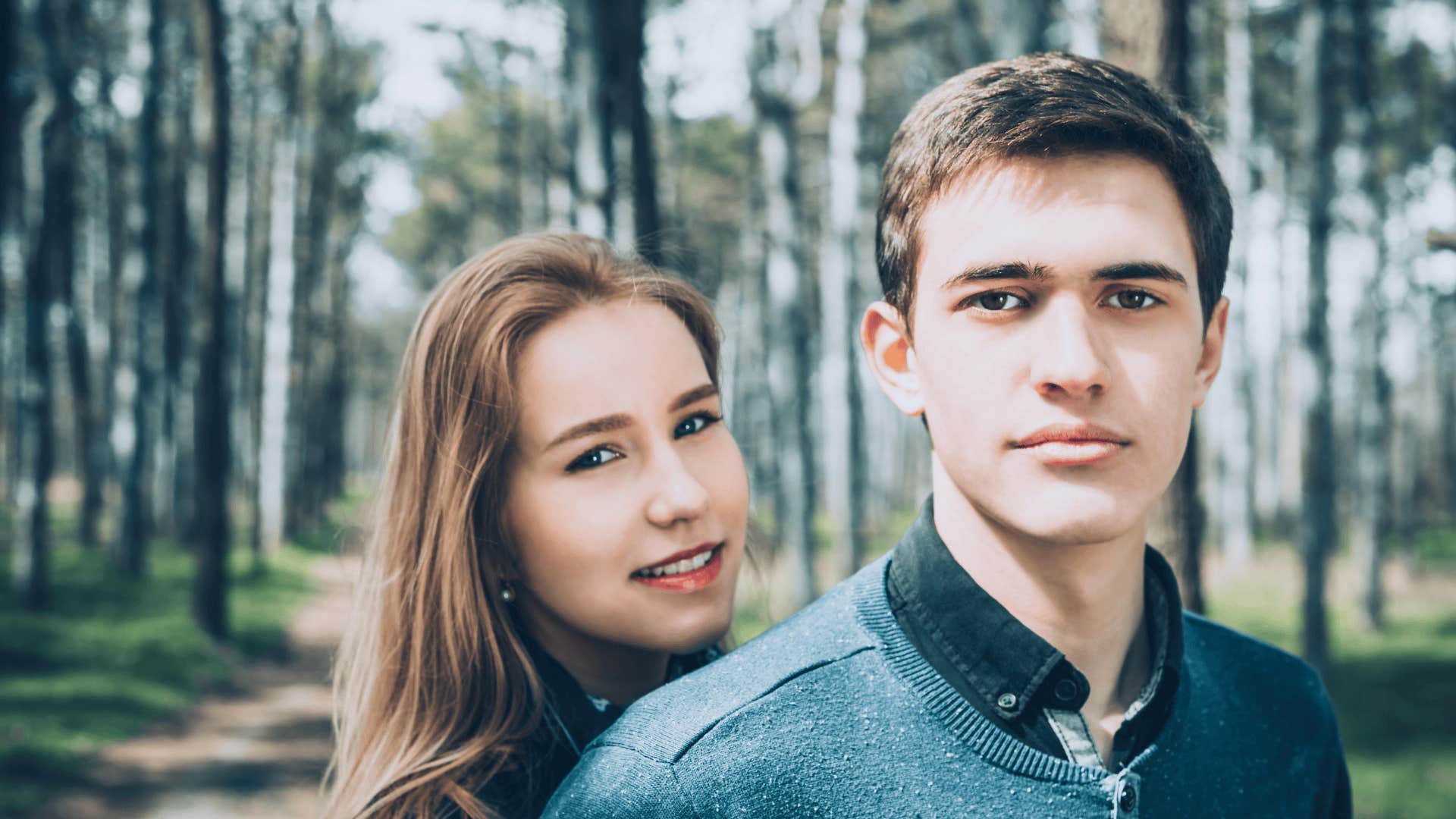 man looking seriously at the camera while a woman smiles behind him