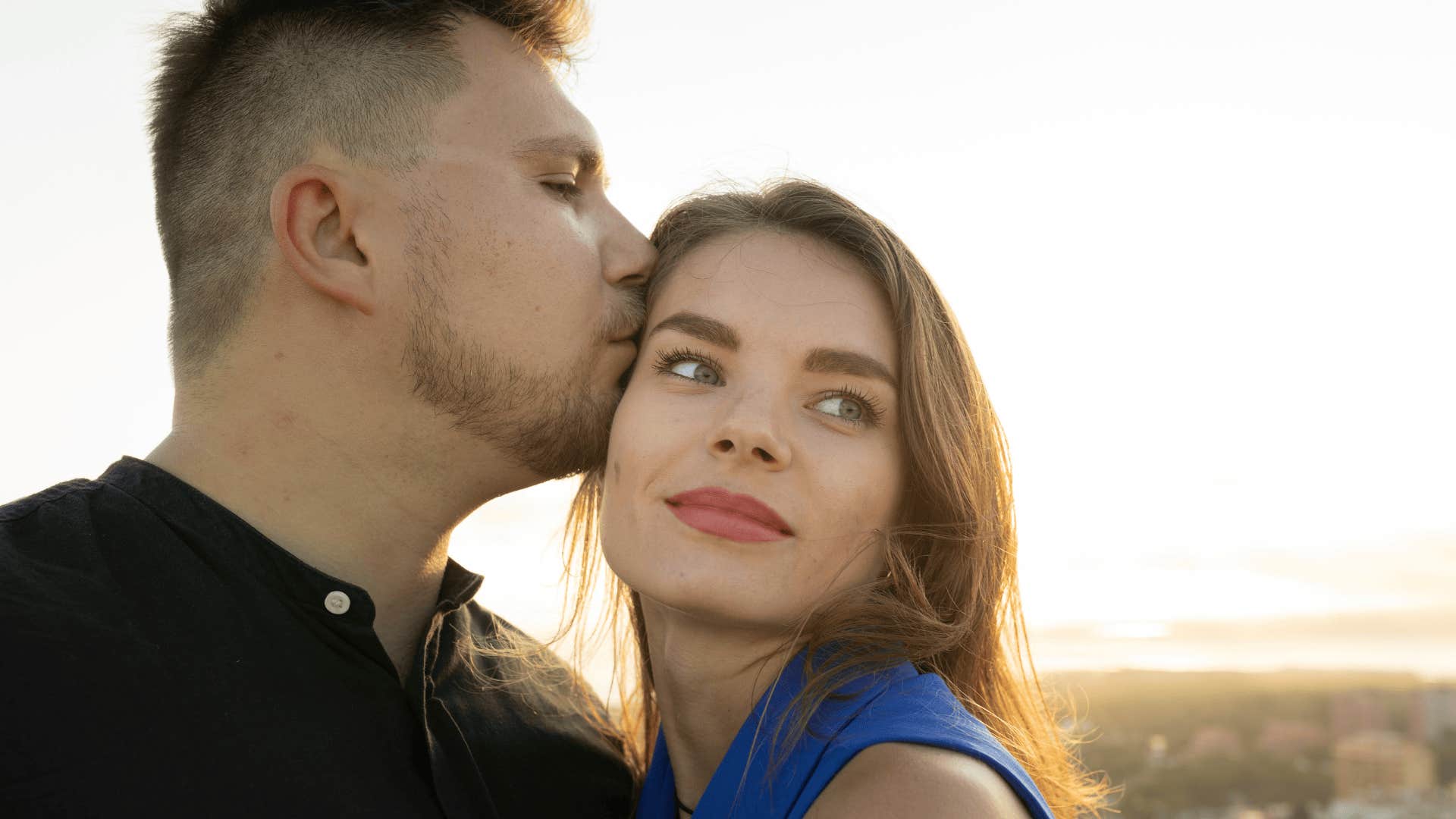 man kissing his wife on the head while she looks off into the distance