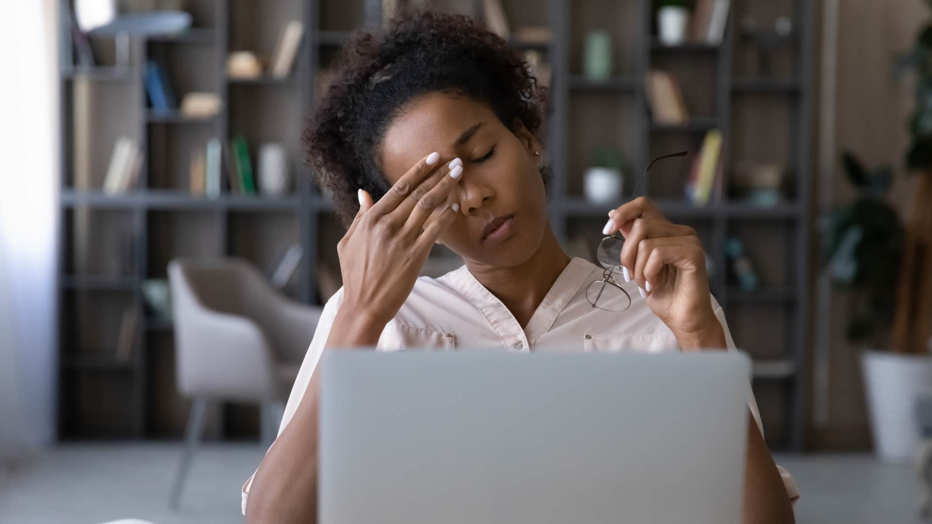 Gen Z woman holding her head while looking at a laptop