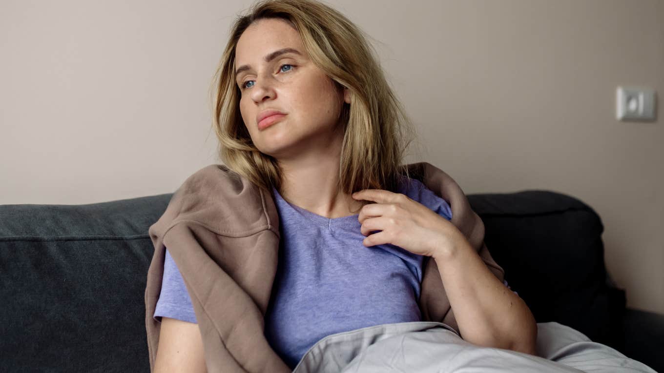 Gen Z woman looking tired sitting on her couch.