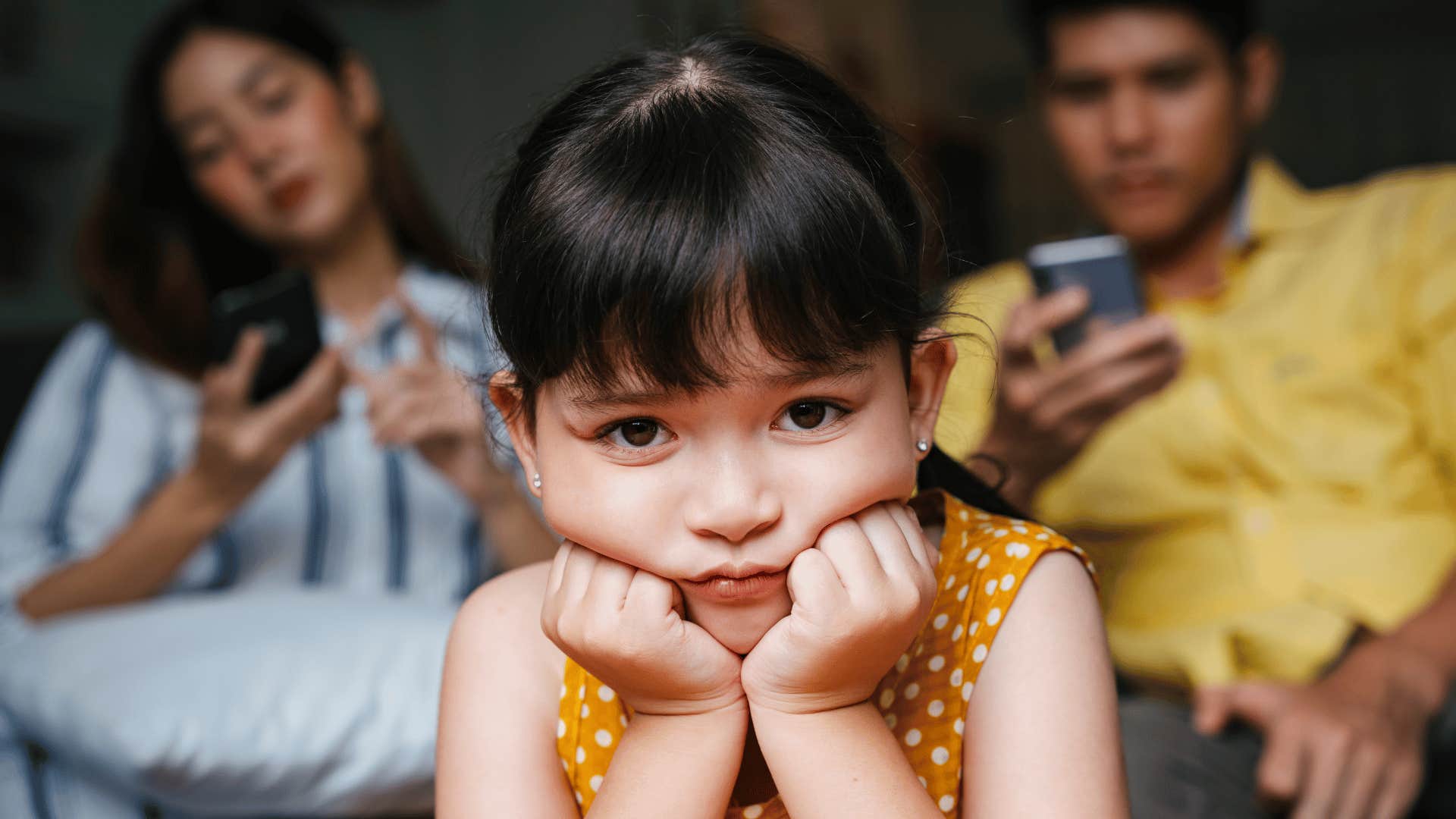 Sad girl waits for parents to stop scrolling on mobile phones