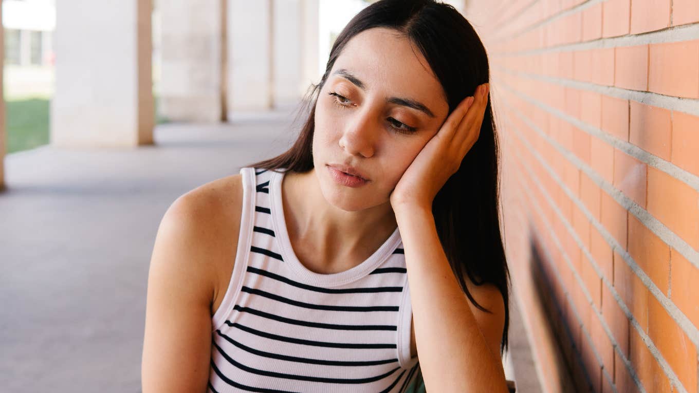 Upset adult child sitting on a bench with her head in her hands.