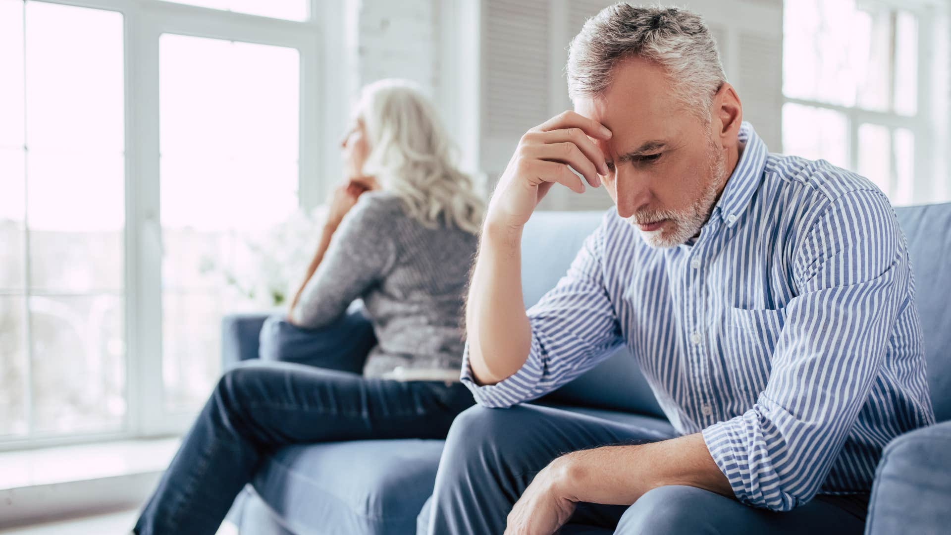 Upset older man holding his head in his hands on a couch