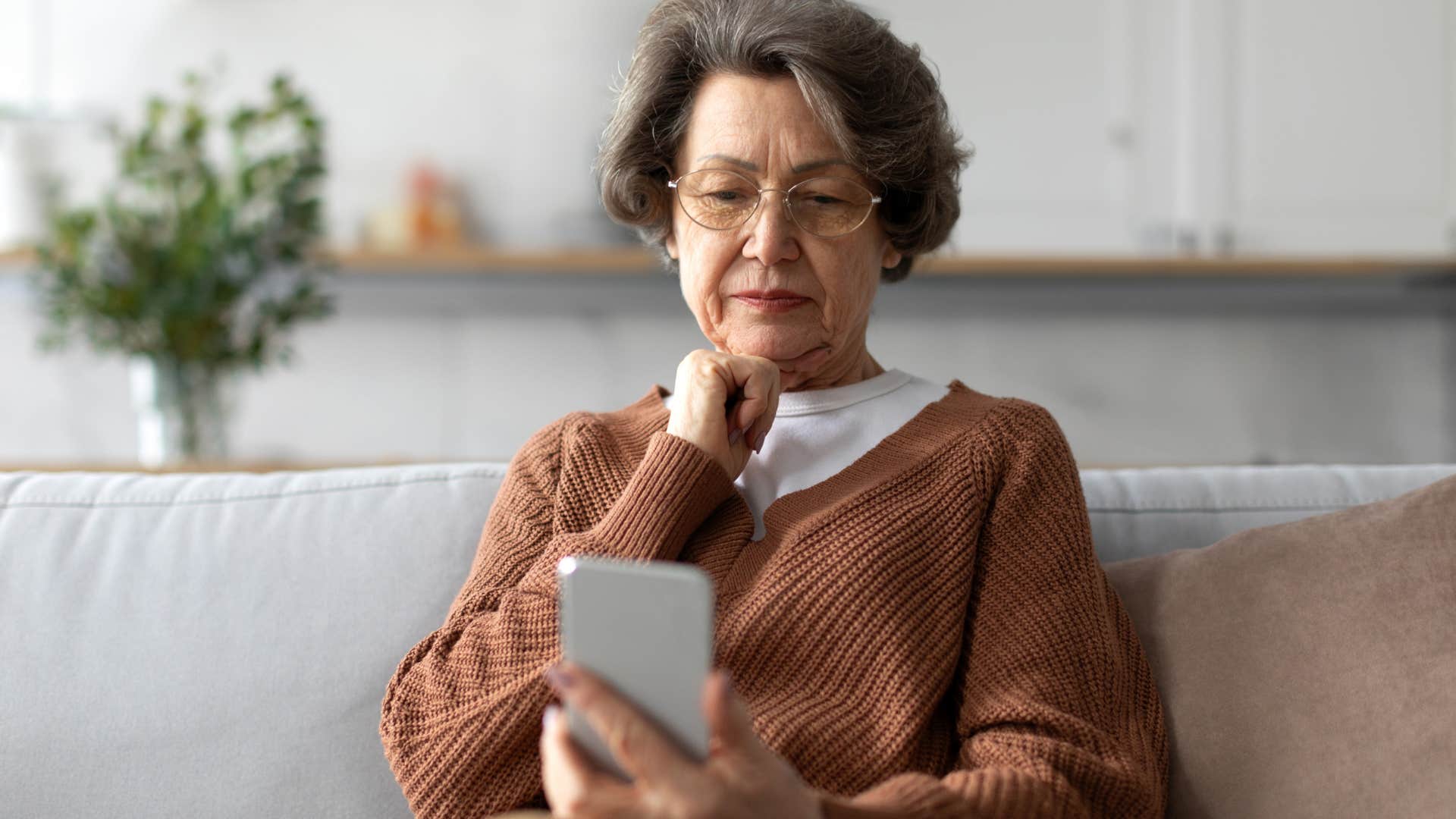 Upset older woman looking at her phone on the couch.