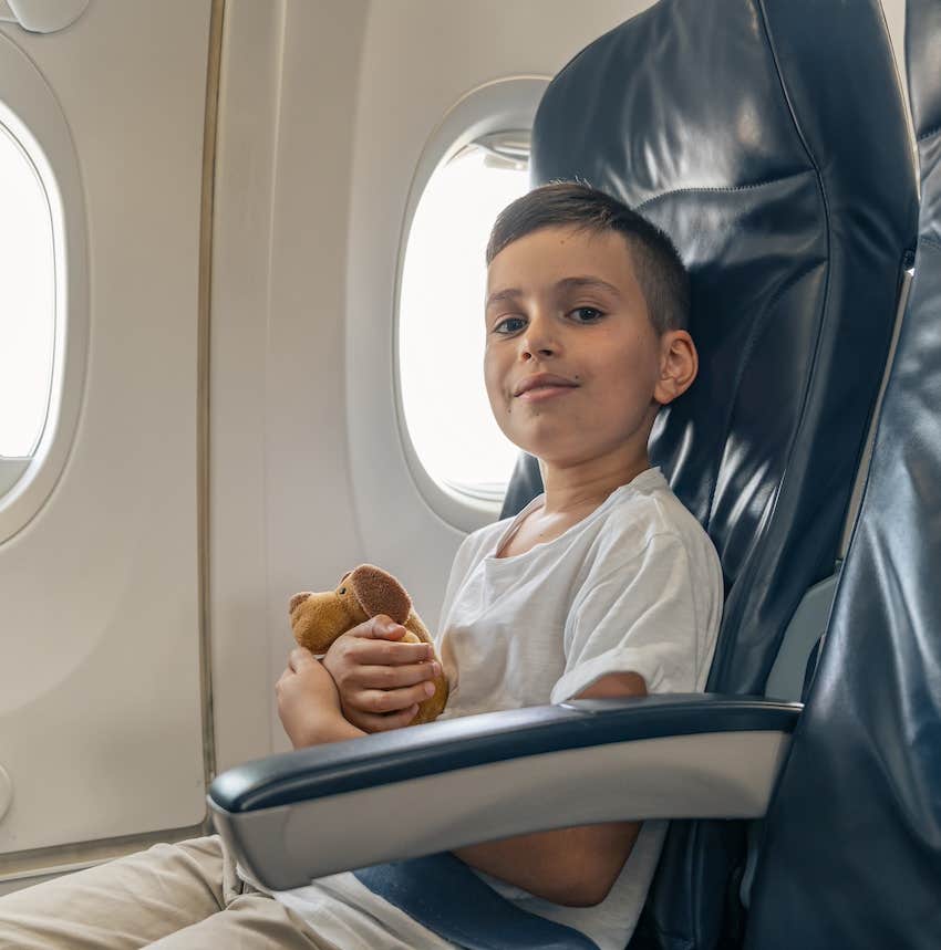 Boy sits in airplane seat and grins mischievously 