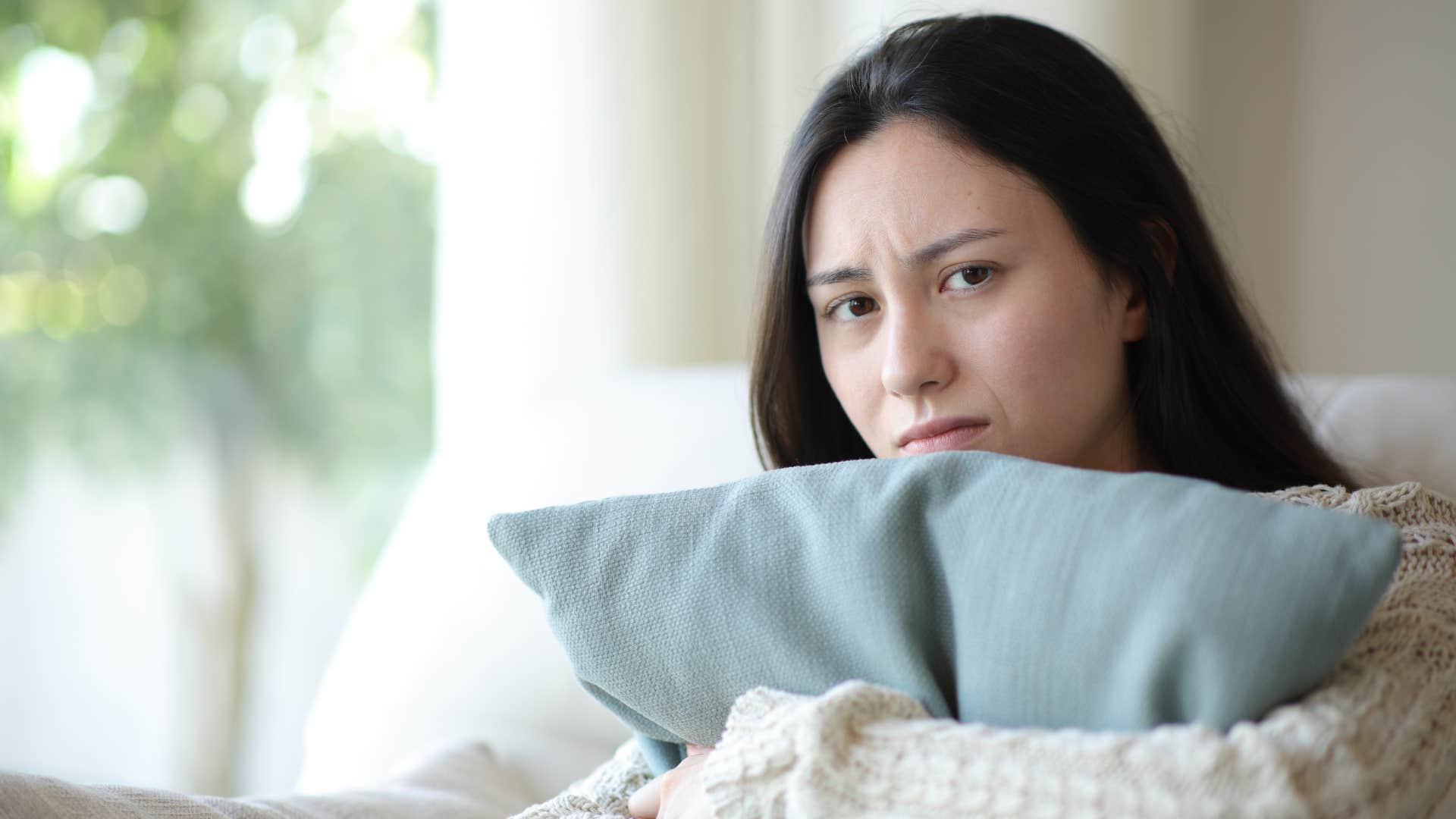 sad woman sitting down hugging pillow