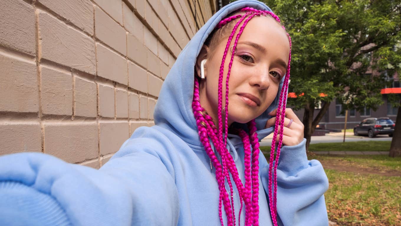 smiling teenager with pink braids taking photo of herself