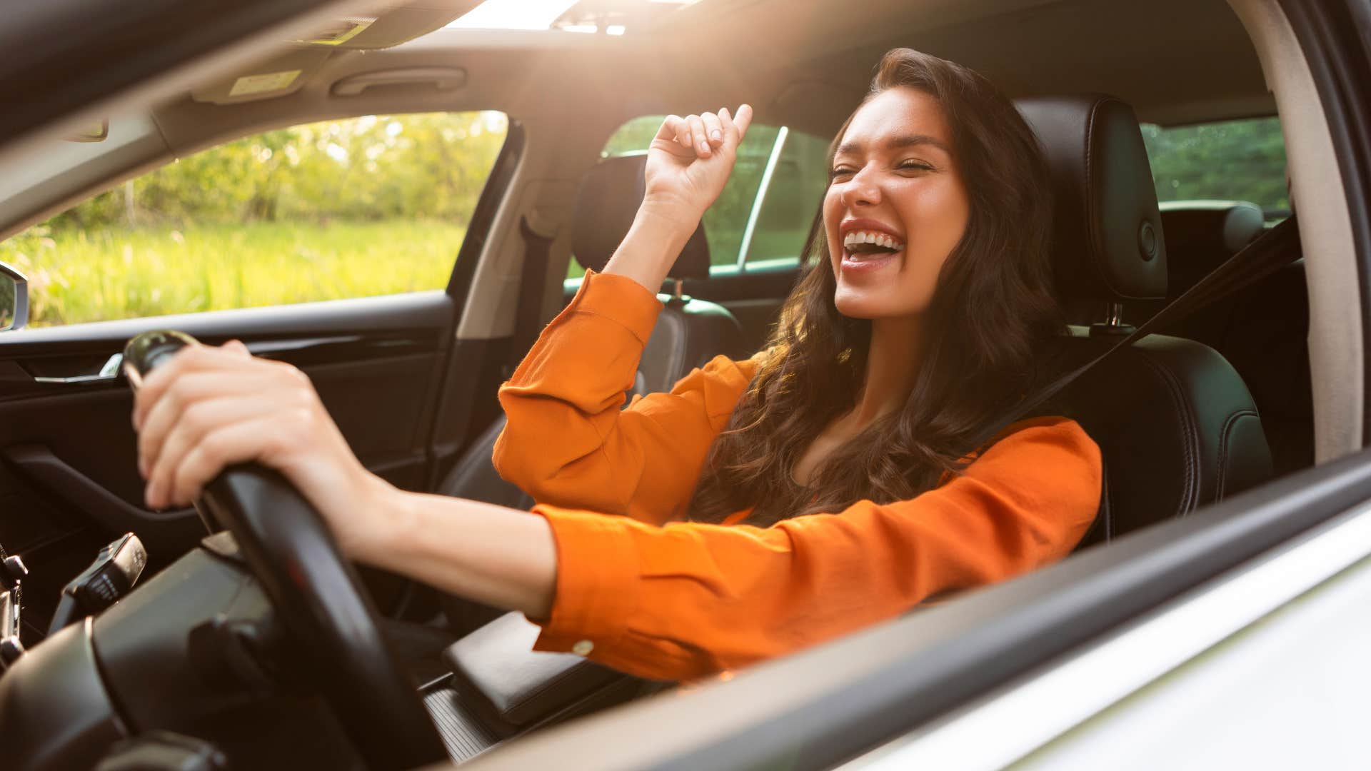 Overjoyed woman driver listening to music and singing while holding one hand on steering wheel