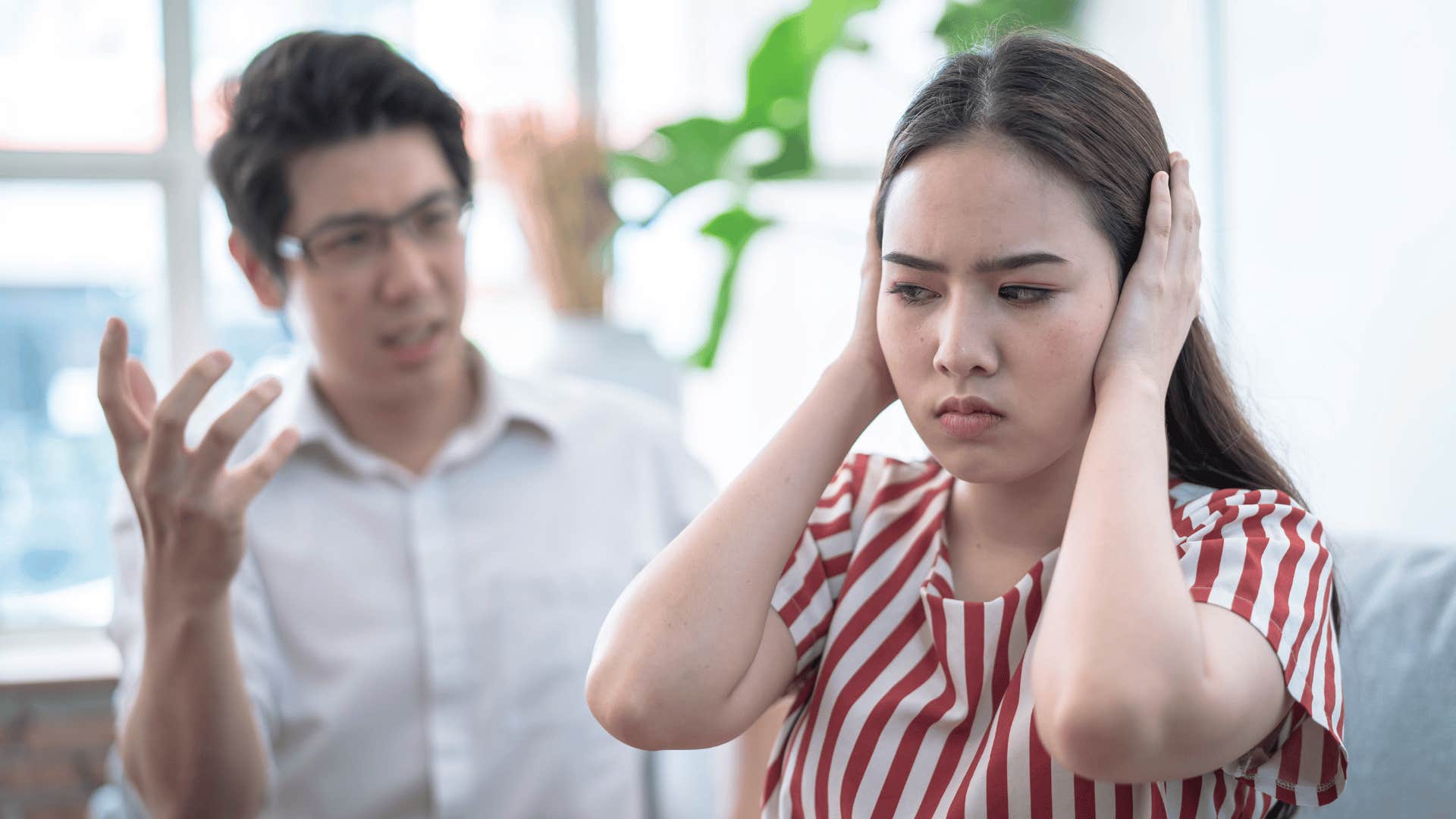 man talking to woman with hands over ears