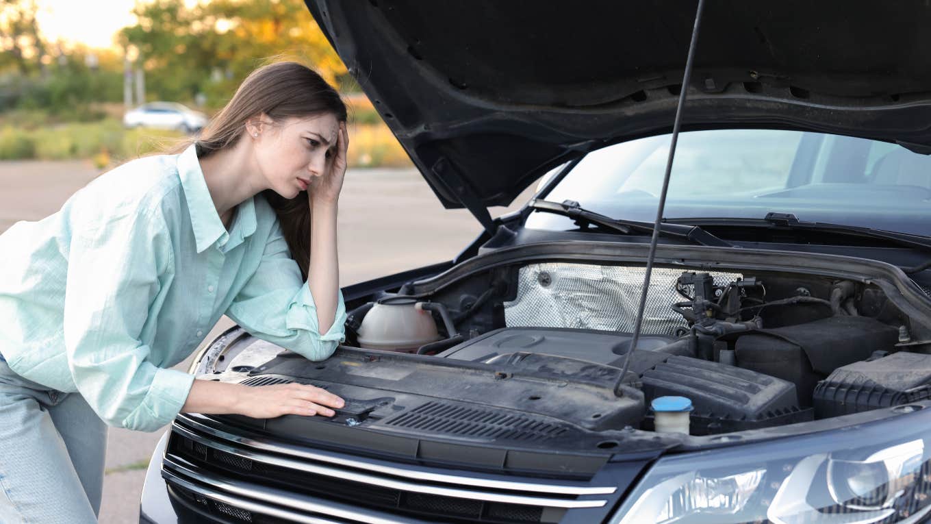 worried woman looking under hood of car 