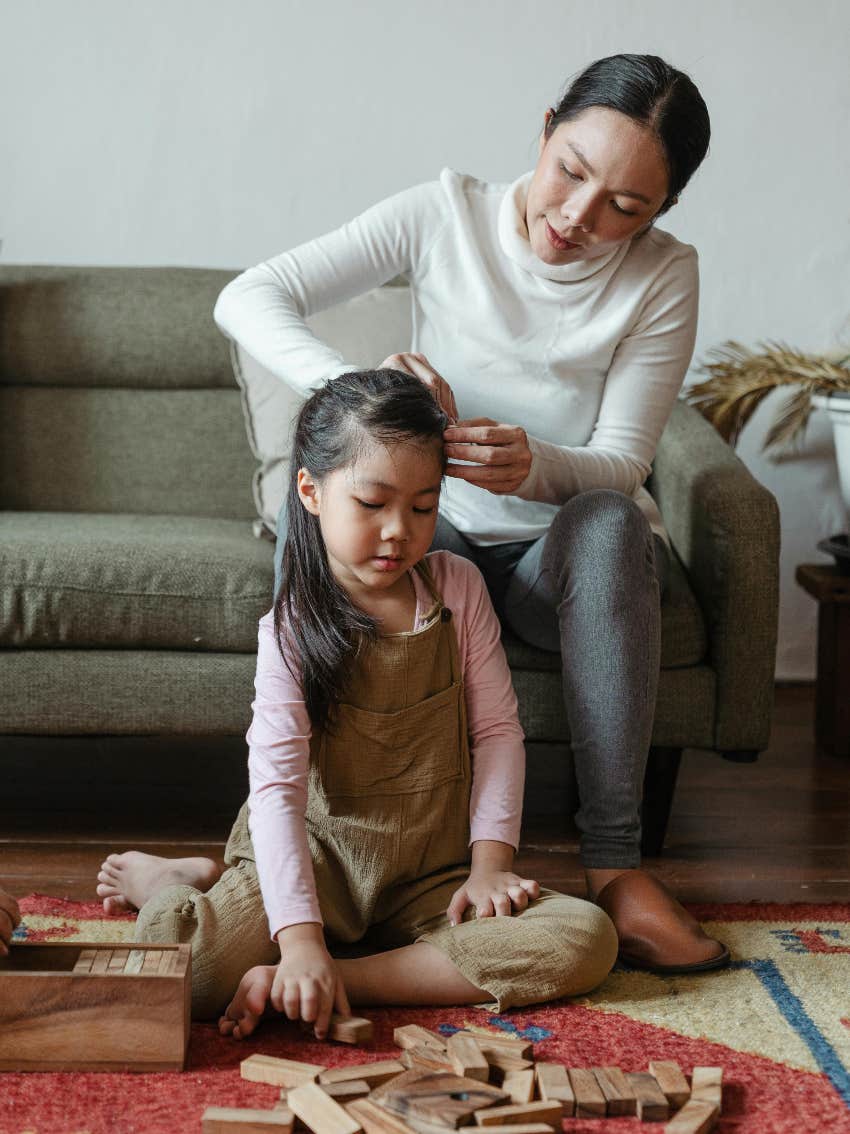 mom doing her daughter's hair while she sits on the floor in front of her