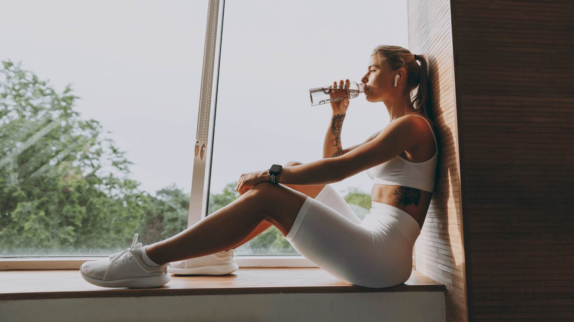 woman wearing white drinking detox on windowsill