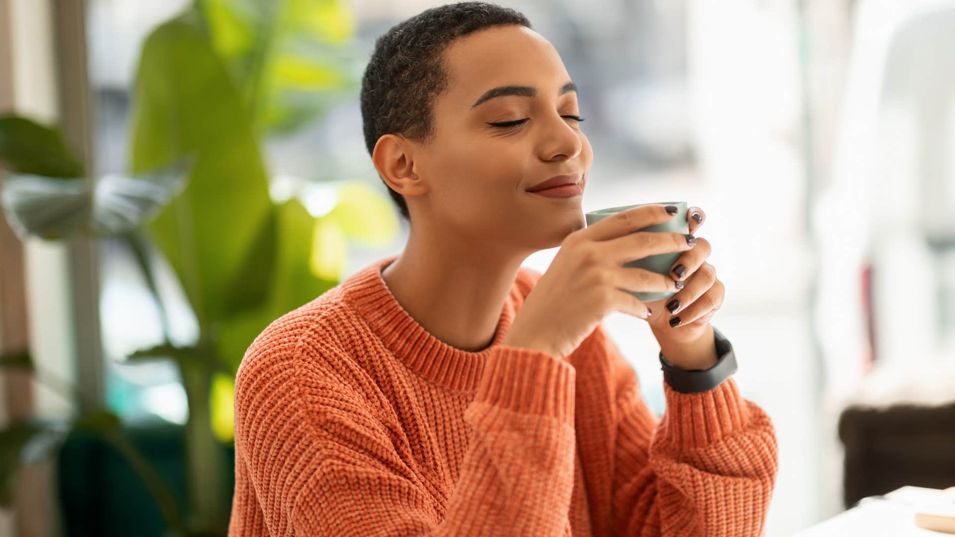 Woman smiling and drinking coffee alone at home.