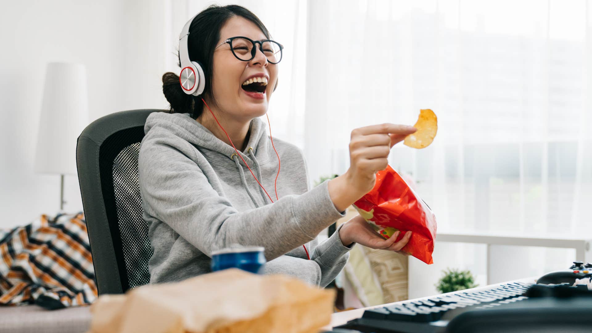 Woman smiling and playing video games in a messy room.