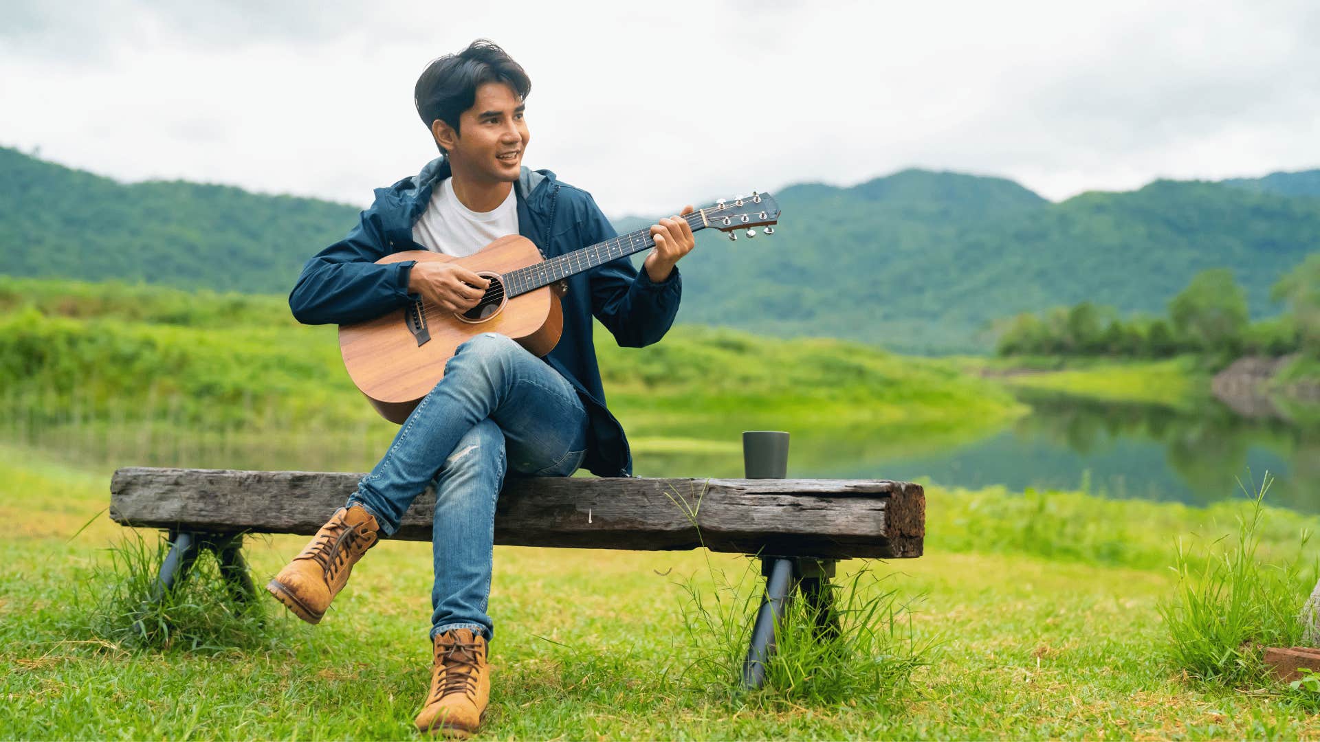 man playing the guitar outside on a bench