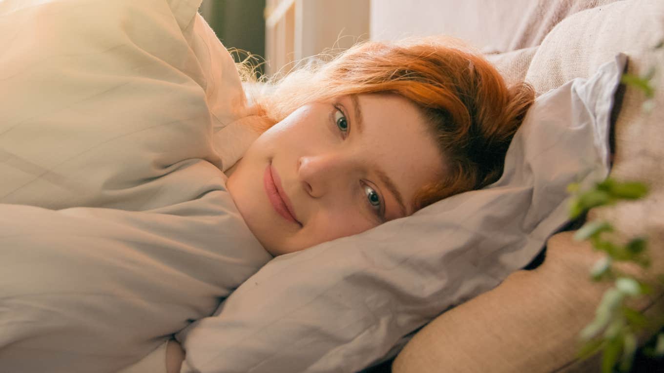 Sleepy woman waking up from dreaming in comfortable white bed smiling 