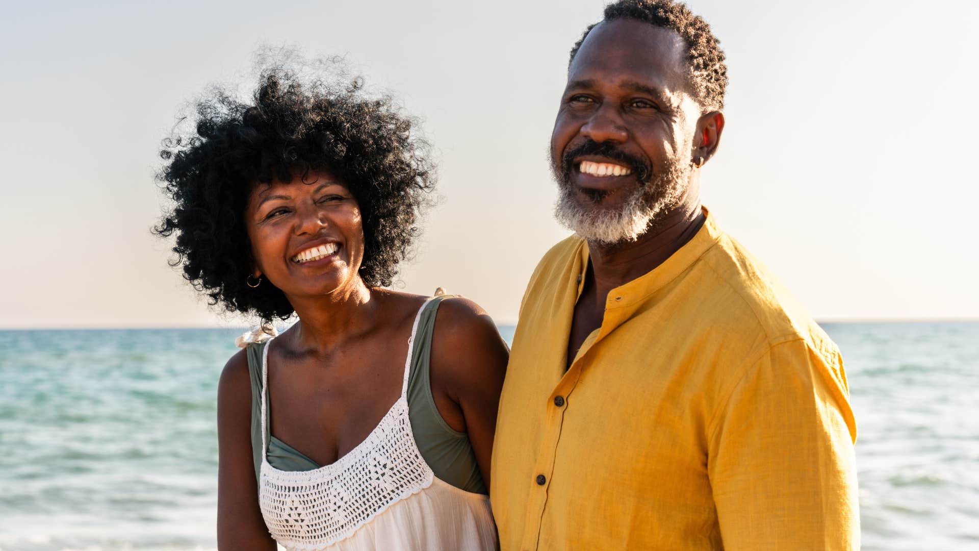 Couple smiling and standing together on a beach.