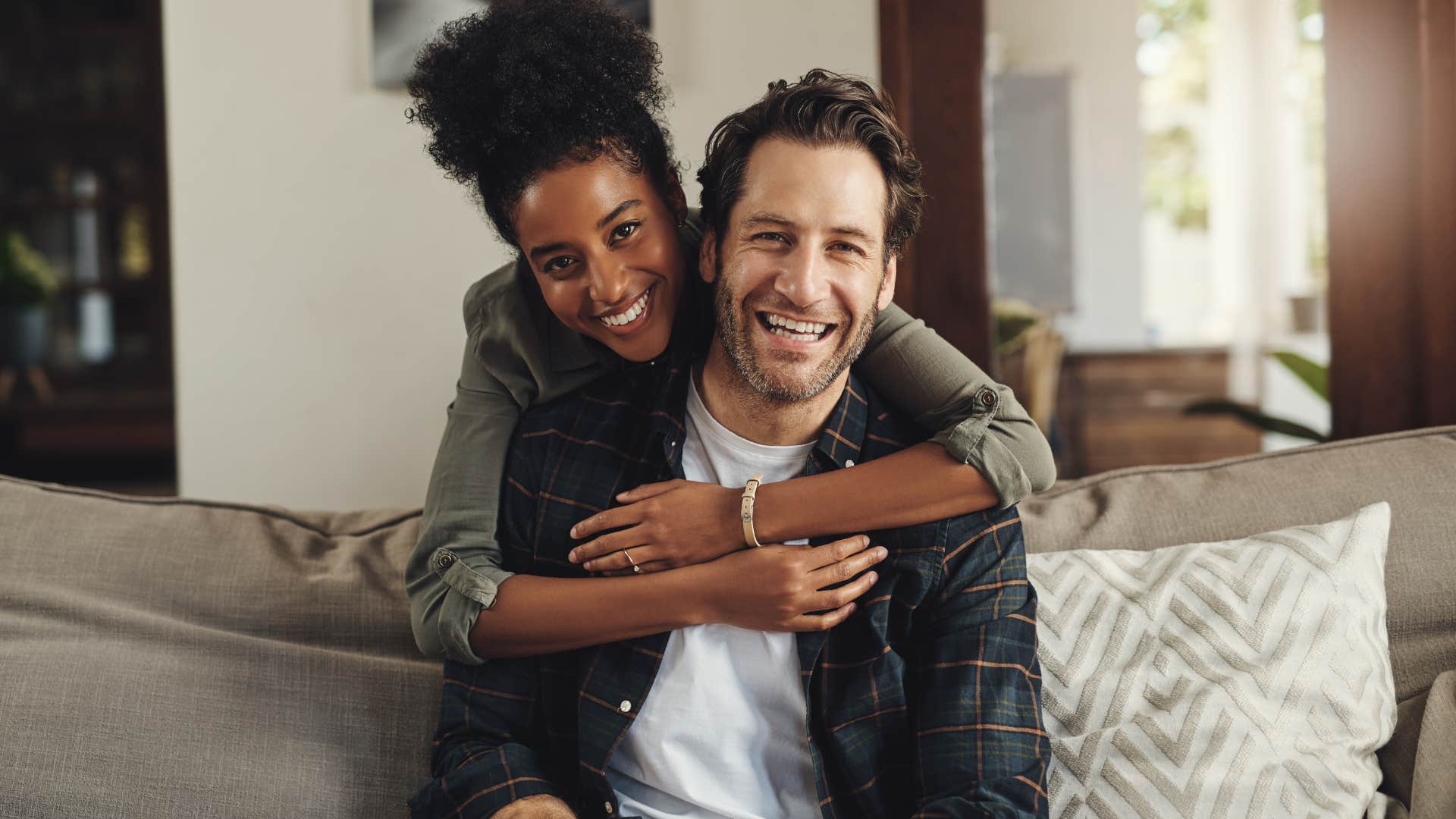 Woman hugging her partner from behind and smiling.