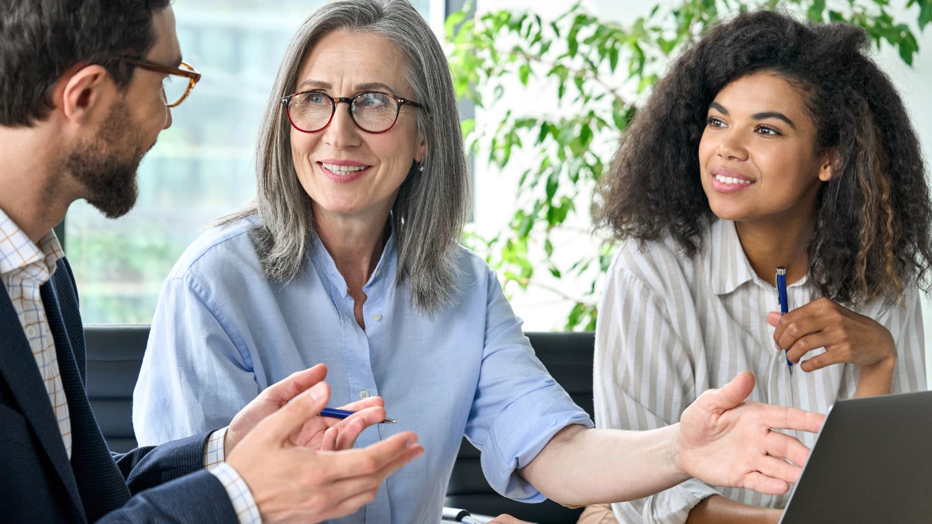 Boomer woman talking to Gen Z co-workers at a desk