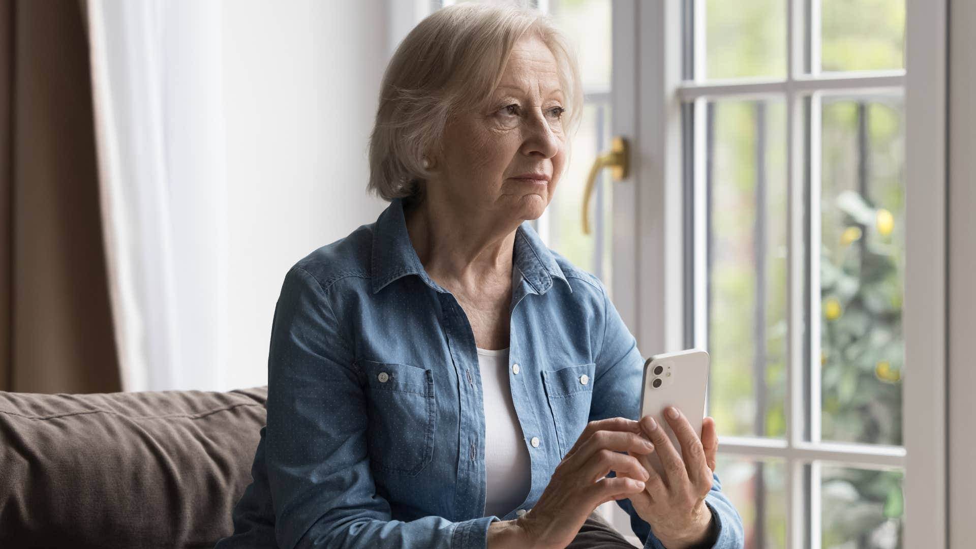 boomer woman sitting on a couch texting on her phone