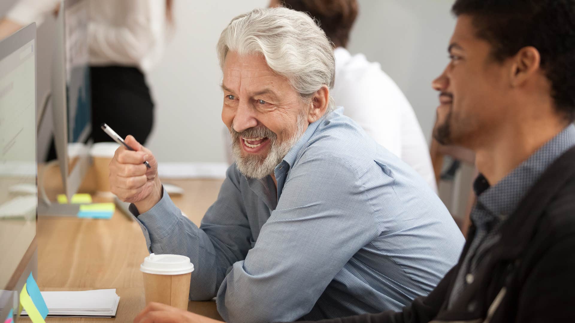 Older man laughing with co-workers at a desk