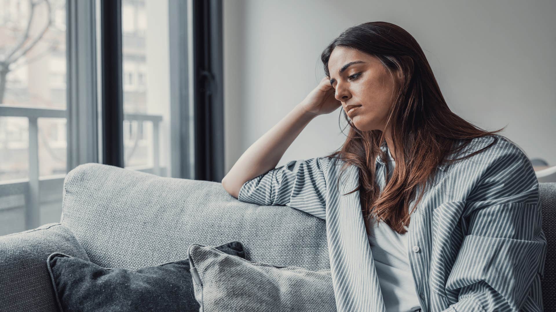 upset woman sitting on couch looking out window