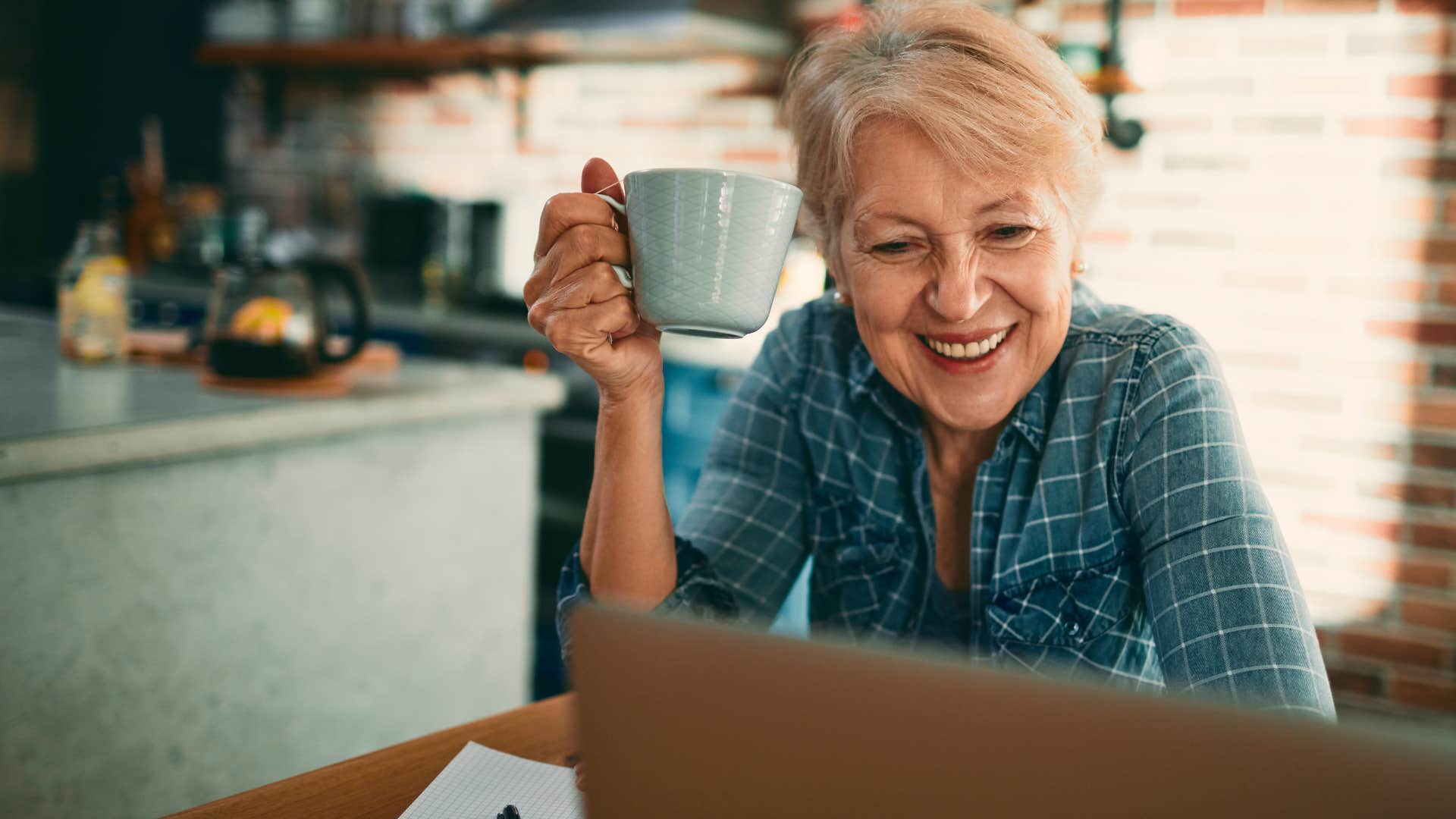 Older woman smiling while looking at her laptop.