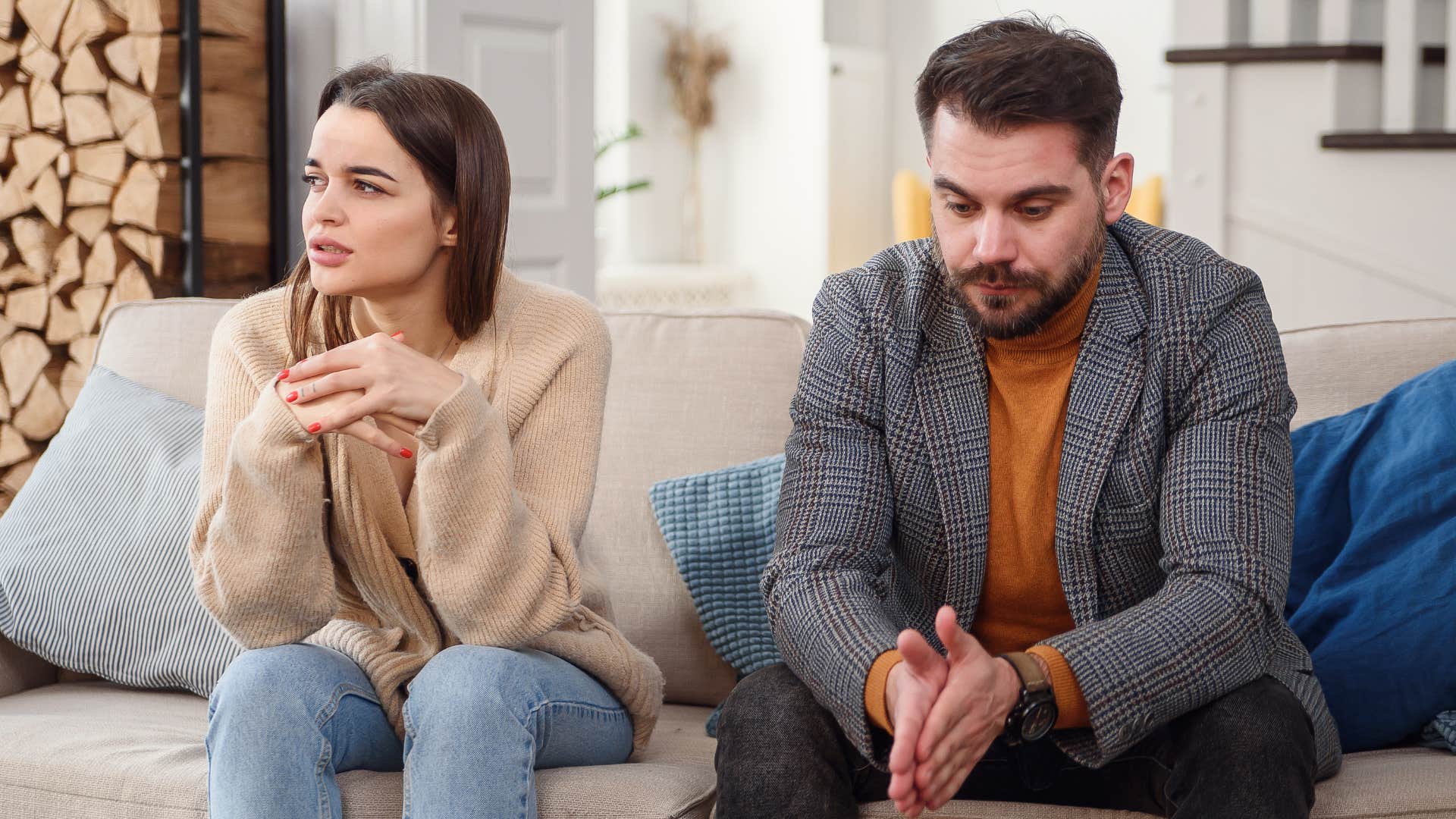 Couple looking upset sitting beside each other on a couch.